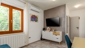 Une chambre moderne dotée d’une grande fenêtre, d’un téléviseur à écran plat fixé au mur, d’une armoire blanche avec des tiroirs et d’un plancher en bois.