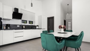 A modern kitchen with white cabinets, a black countertop, and a dining area with green chairs and a white table. - Three Bedroom Villa with Swimming Pool (Labin)
