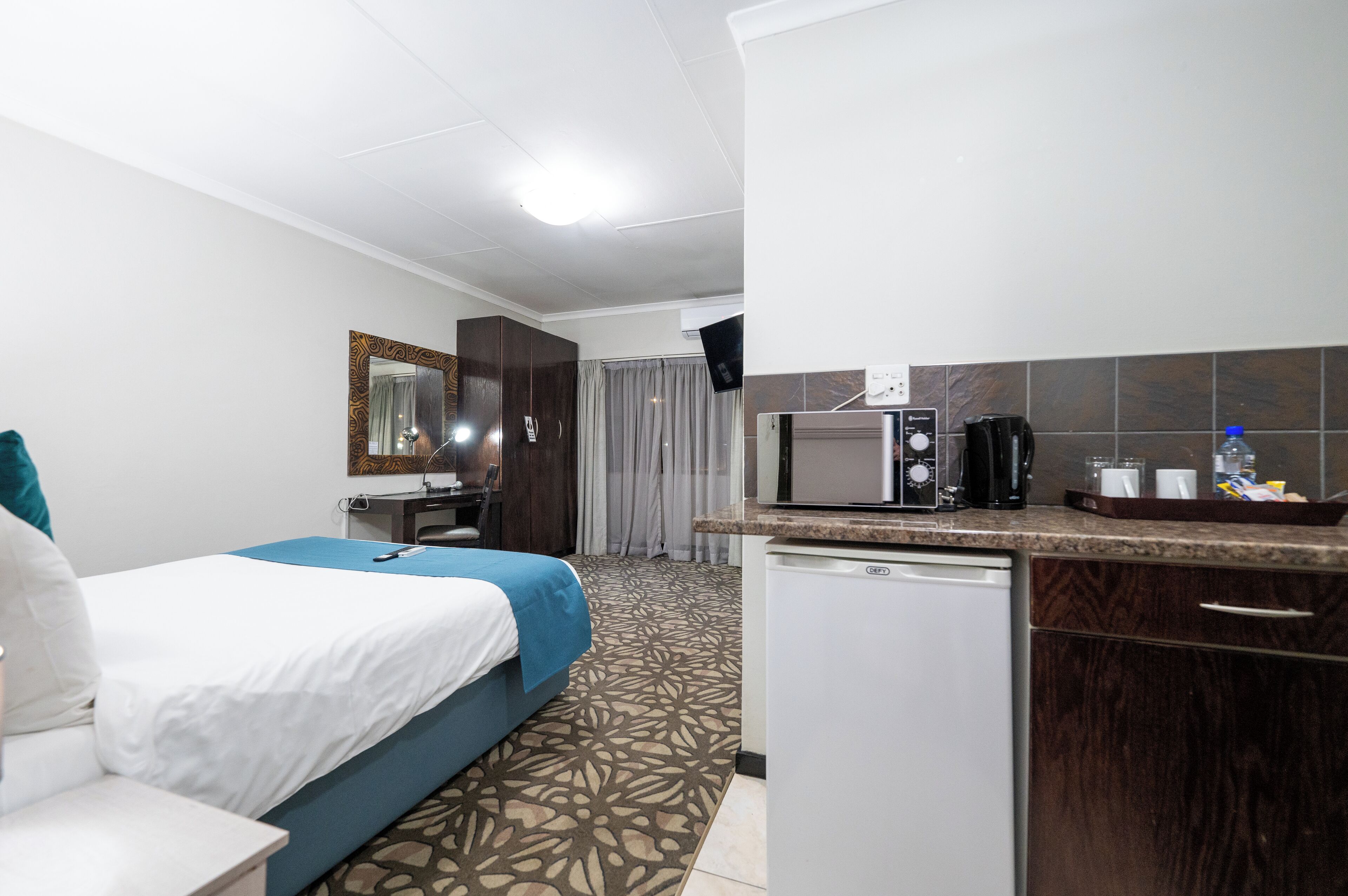 A hotel room with a bed, a desk, a microwave, a coffee maker, and a small refrigerator.