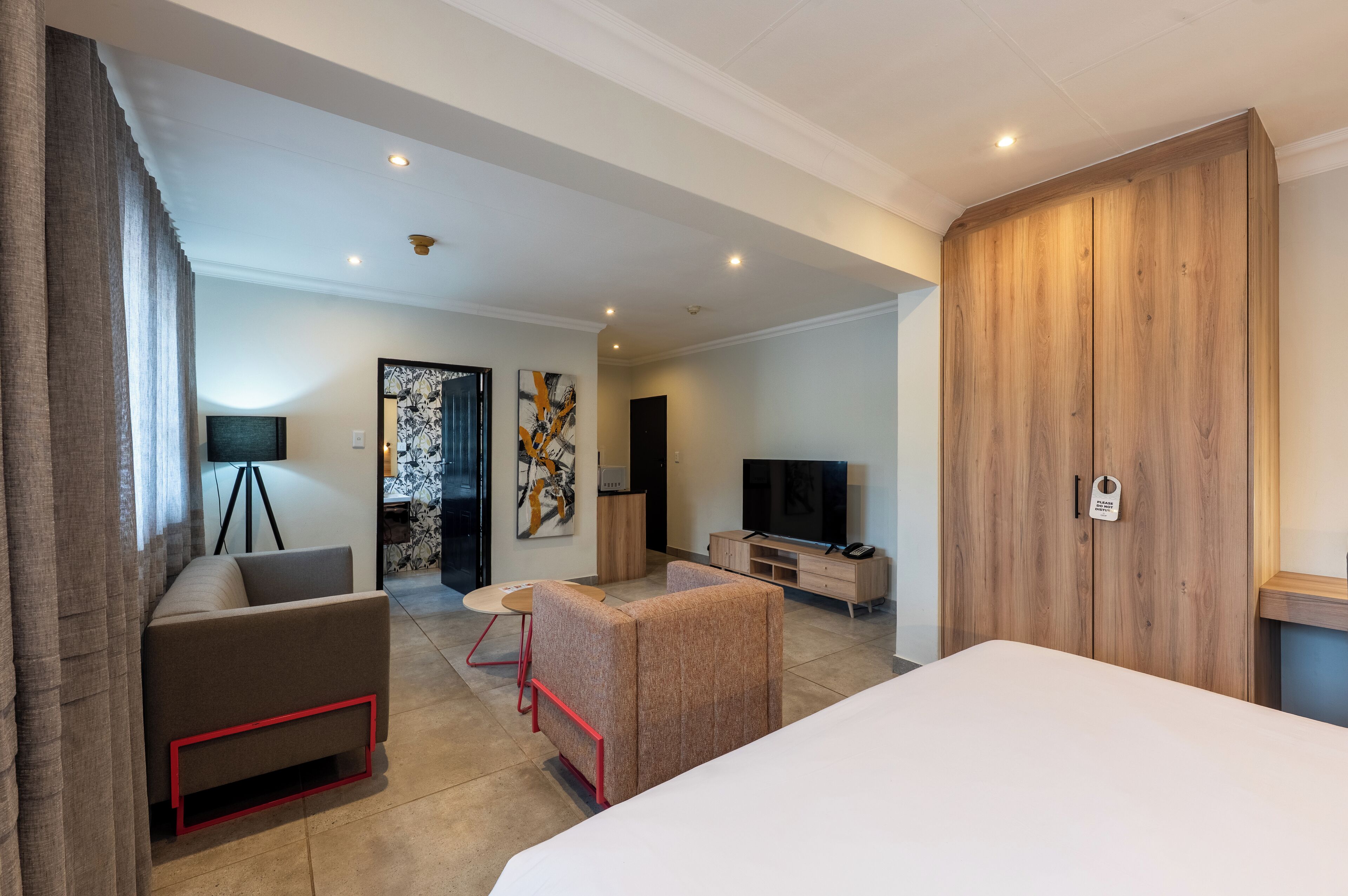 A modern hotel room with a bed, a sofa, a TV, and a wooden wardrobe.