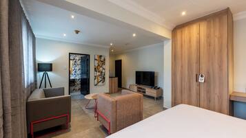 A modern hotel room with a bed, a sofa, a TV, and a wooden wardrobe.
