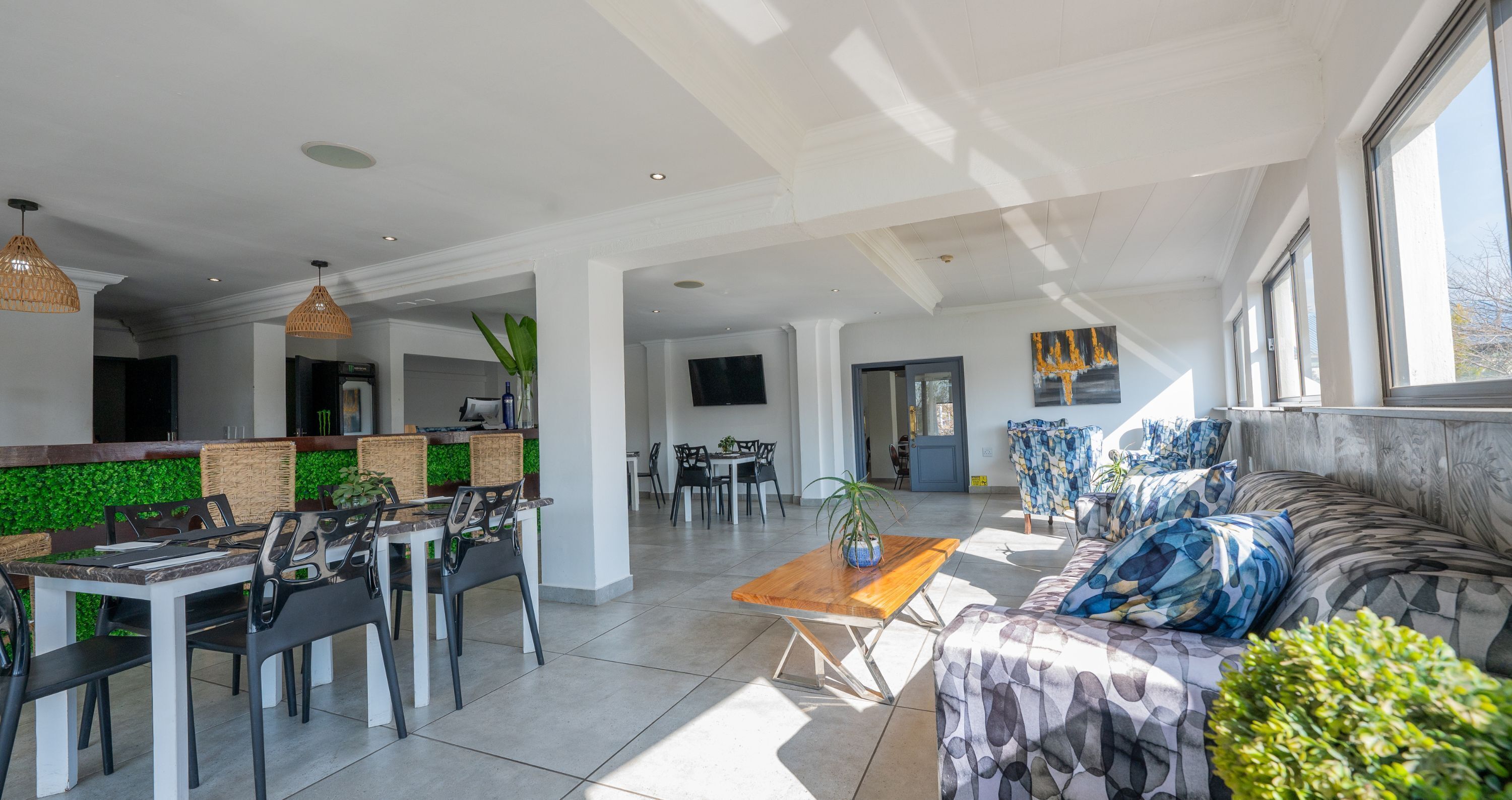 Amplia sala de estar con sofá, mesa de comedor, sillas y mesa de centro. Se observa una cocina al fondo con mostrador y sillas.
