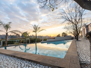 A swimming pool with a tiled border, surrounded by trees and a sunset view. - ANEW Hotel & Convention Centre OR Tambo (Benoni)
