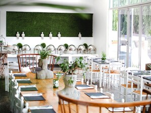 A dining area with white tables and chairs, a green wall, and potted plants. - ANEW Hotel & Convention Centre OR Tambo (Benoni)