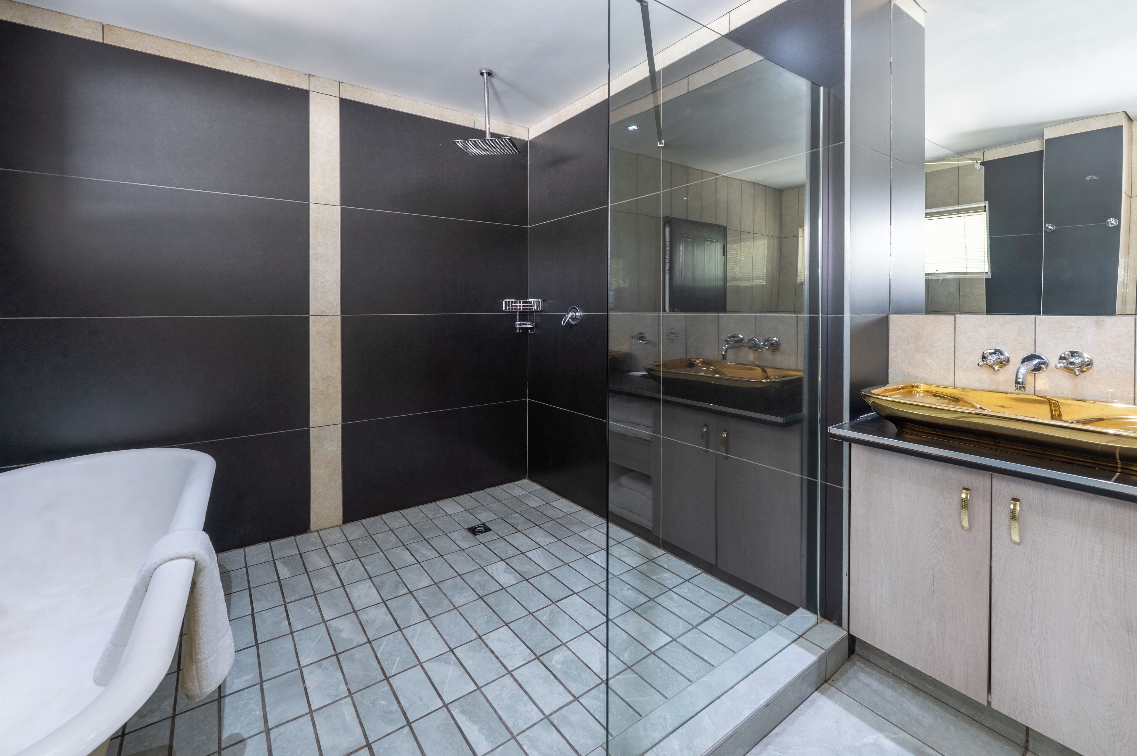 Een moderne badkamer met een douchecabine van glas, een witte badkuip en een wastafelmeubel met wastafel en spiegel.