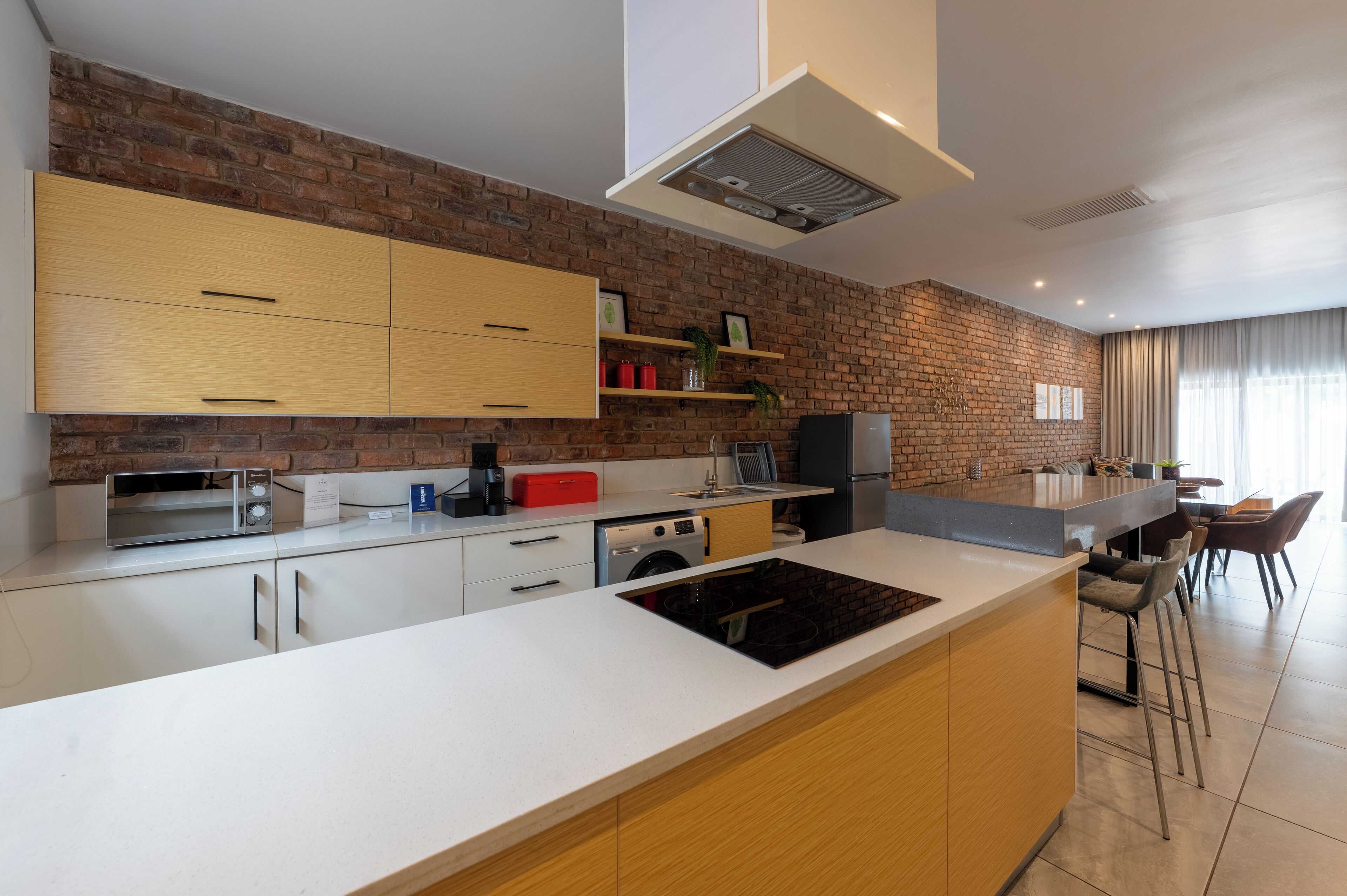 A modern kitchen with a brick wall, wooden cabinets, a built-in oven, and a bar area with stools.