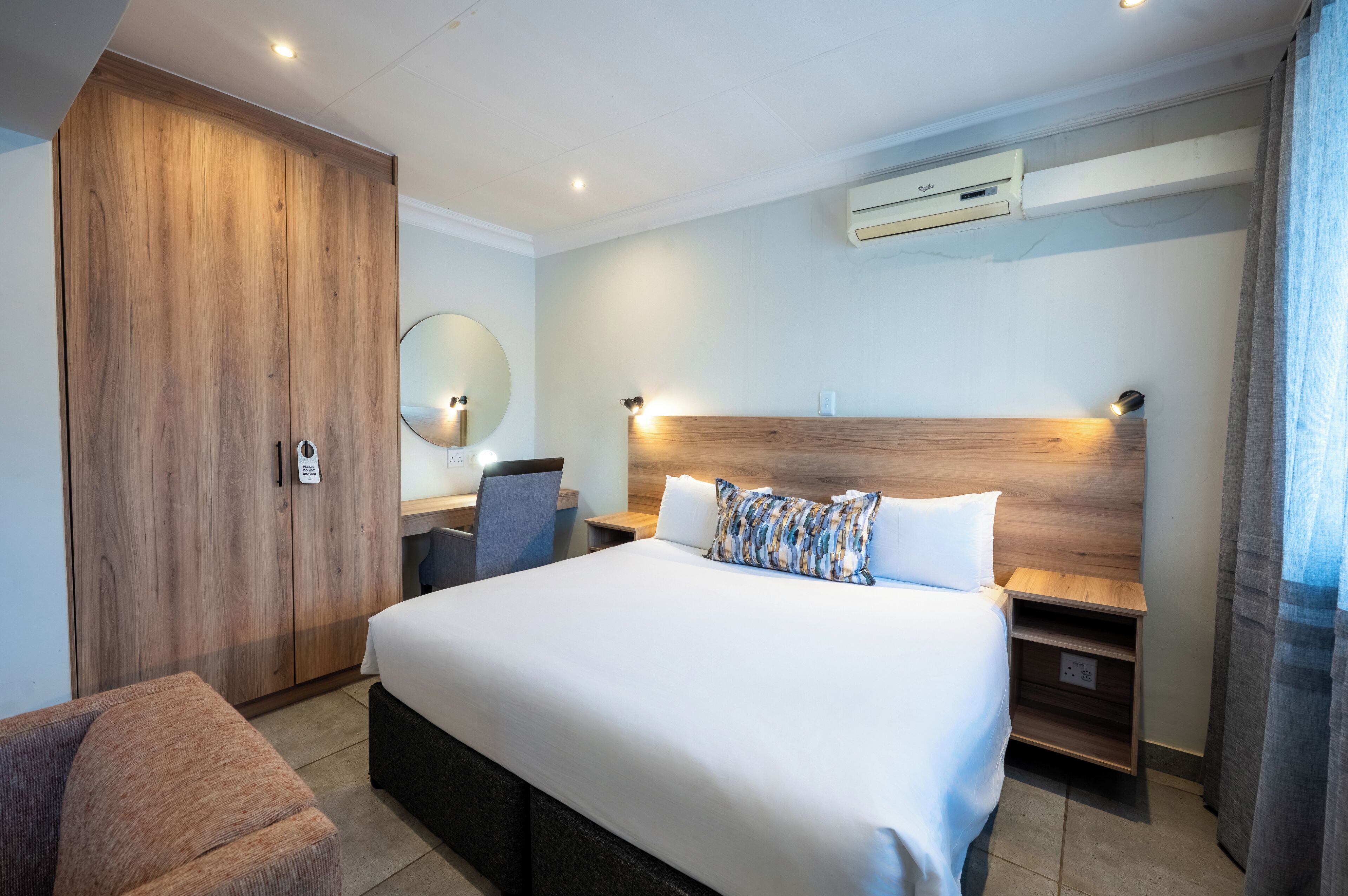 Une chambre d’hôtel avec un grand lit, une armoire en bois, un bureau avec une chaise et une table de chevet.