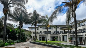 A hotel courtyard with palm trees, a stone pathway, and a building with multiple balconies. - ANEW Hotel & Convention Centre OR Tambo (Benoni)
