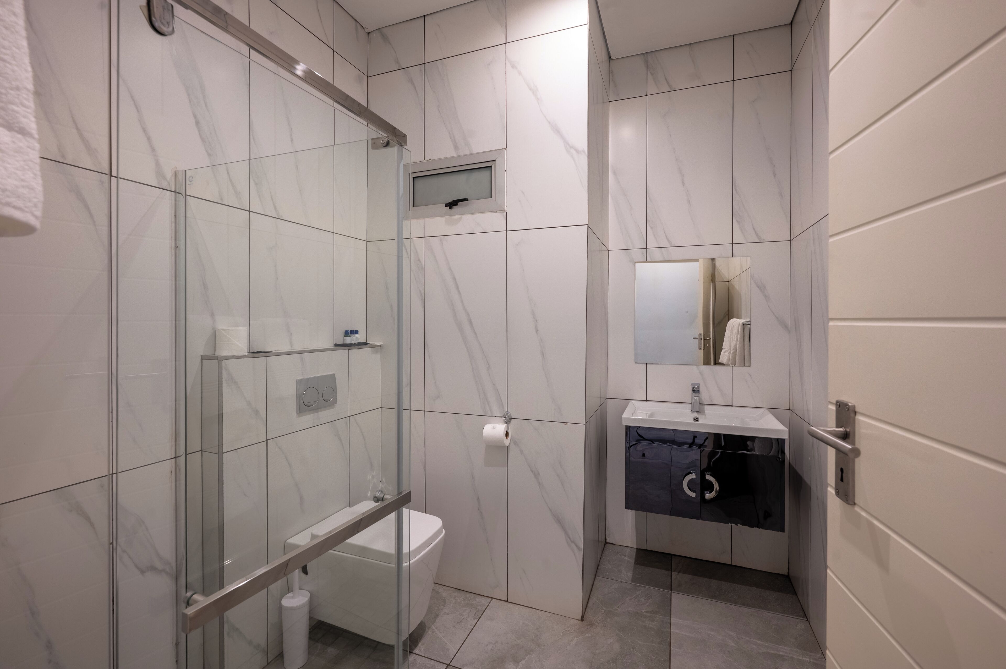 A modern bathroom with a glass shower enclosure, a toilet, a sink with a mirror, and a towel rack.