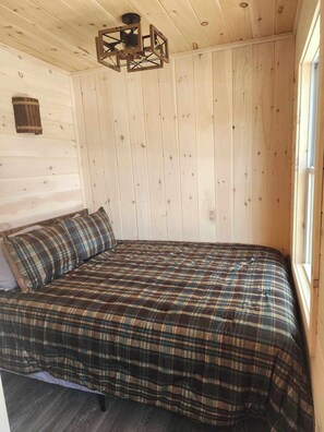 A wooden cabin room with a bed, a window, and a ceiling light fixture.