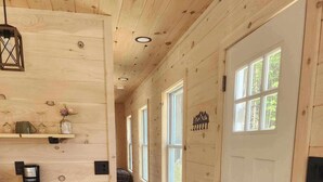 A wooden interior with a kitchen area, white cabinets, a coffee machine, and a hallway leading to a door with windows.
