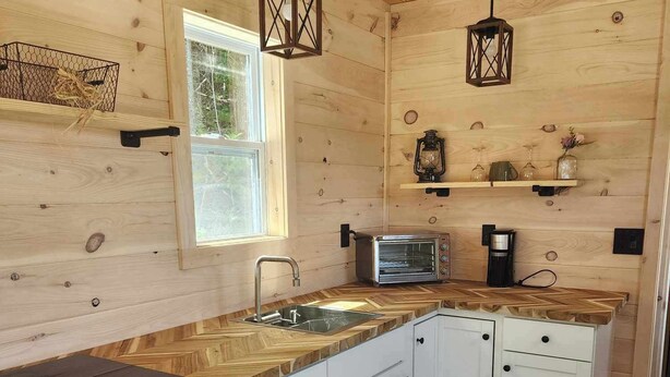 A compact kitchen with wooden walls, a herringbone countertop, and a black refrigerator.