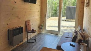 A cabin interior with a ceiling fan, a television mounted on the wall, a sign reading "GATHER", a sofa, a table with a remote control, and a small plant.