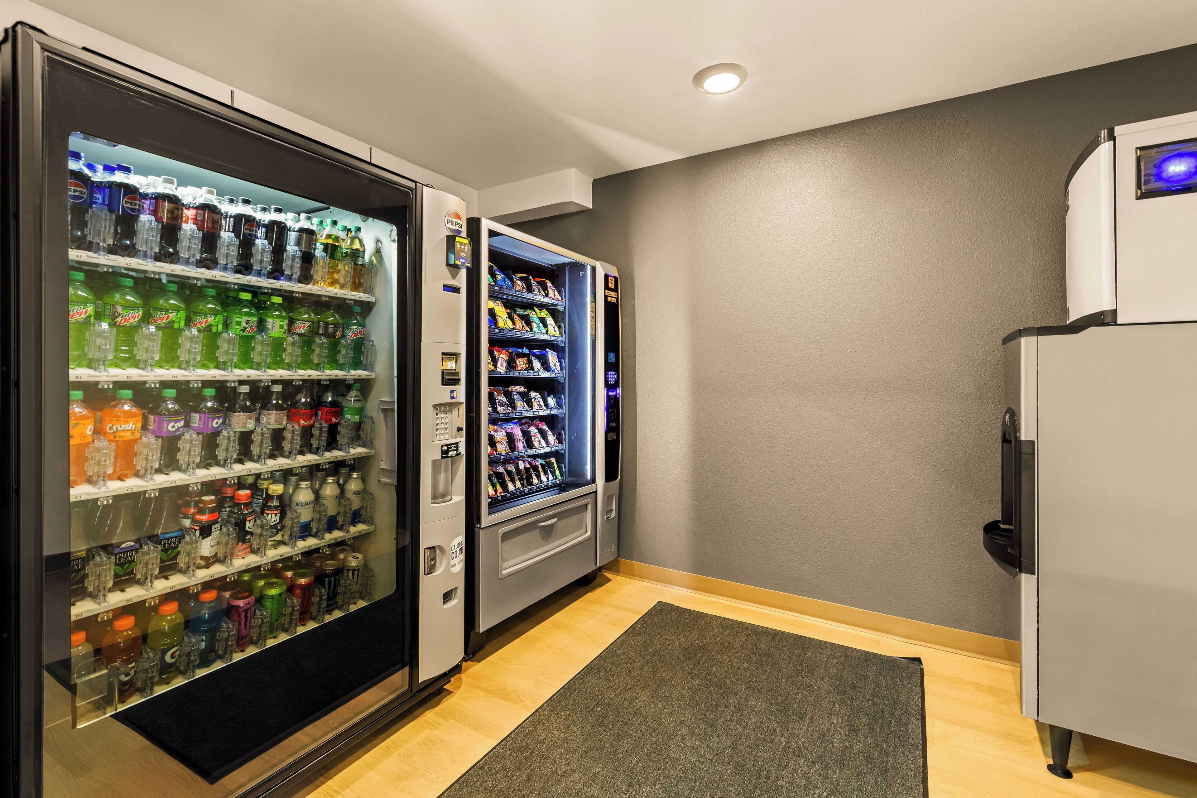 A room with a refrigerator and two beverage vending machines.