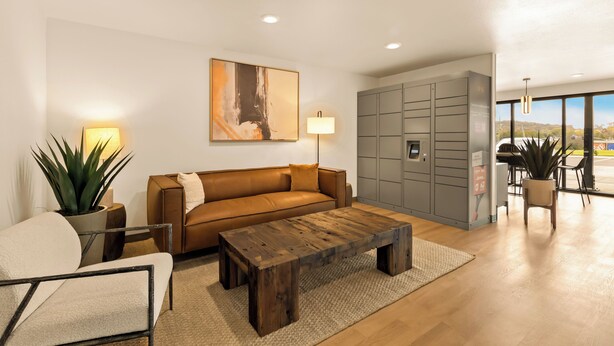 A modern living room with a brown leather sofa, a wooden coffee table, a potted plant, and a large abstract painting on the wall. - LivAway Suites Nashville- Smyrna (Smyrna)