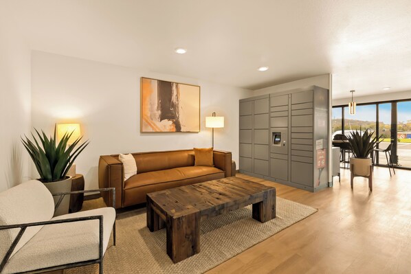 A modern living room with a brown leather sofa, a wooden coffee table, a potted plant, and a large abstract painting on the wall. - LivAway Suites Nashville- Smyrna (Smyrna)