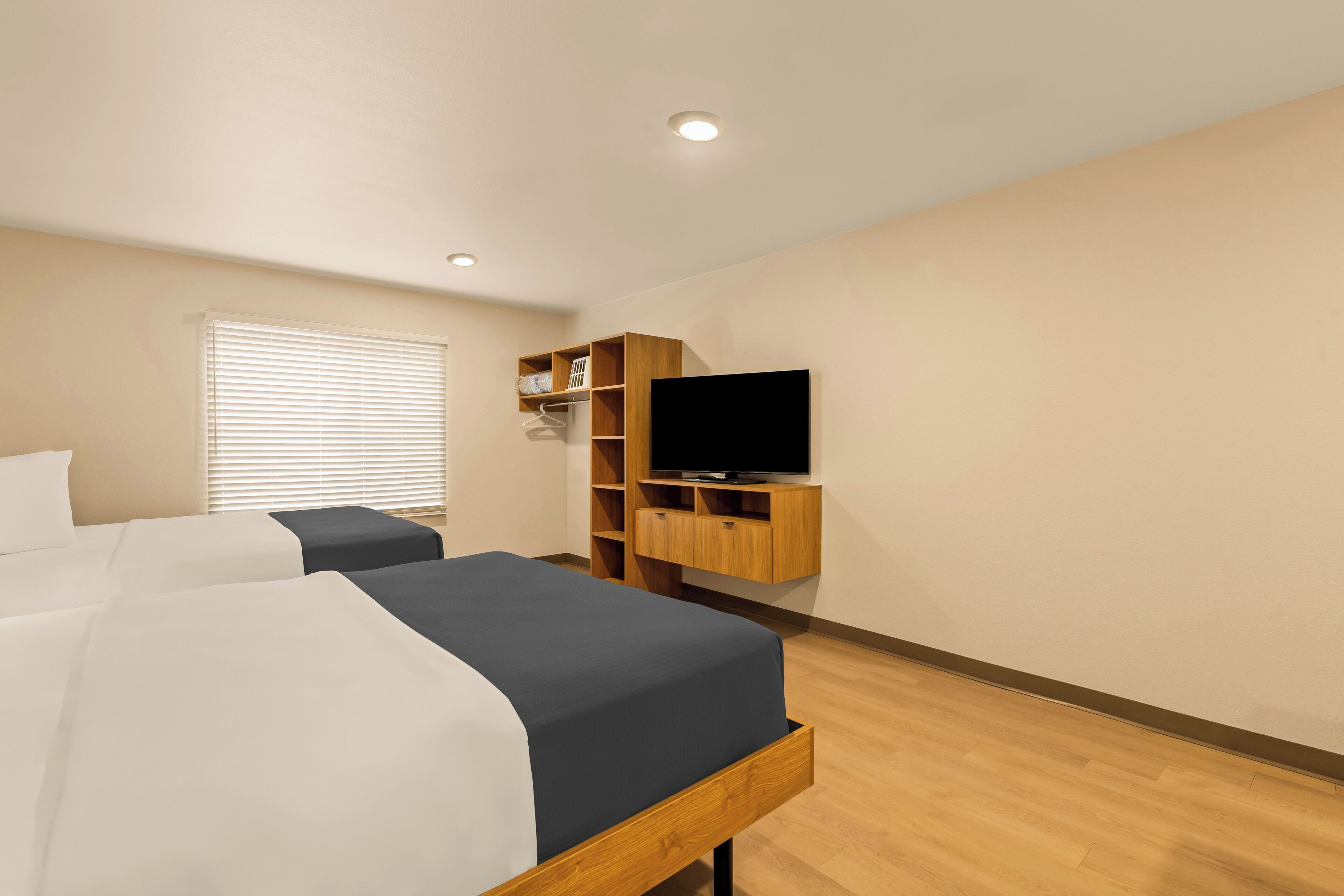 Habitación de hotel con dos camas, televisión y estanterías empotradas.