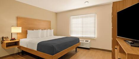 Une chambre d’hôtel avec un lit en bois, une table de chevet avec une lampe, un téléviseur et une fenêtre avec des stores.