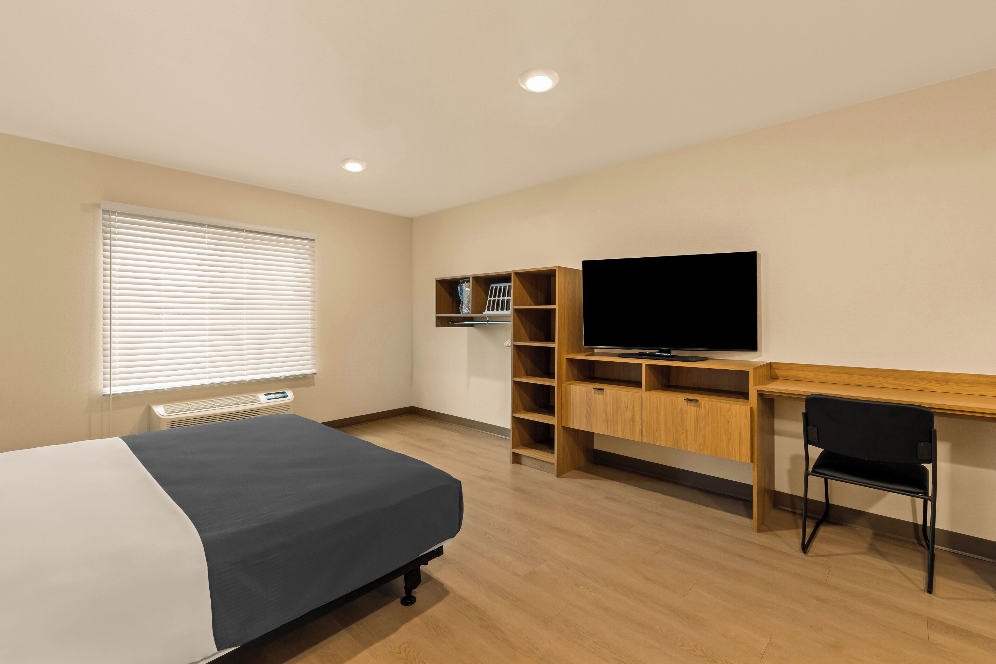Una habitación de hotel con cama, escritorio, televisor y estantería empotrada.