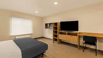Una habitación de hotel con cama, escritorio, televisor y estantería empotrada.