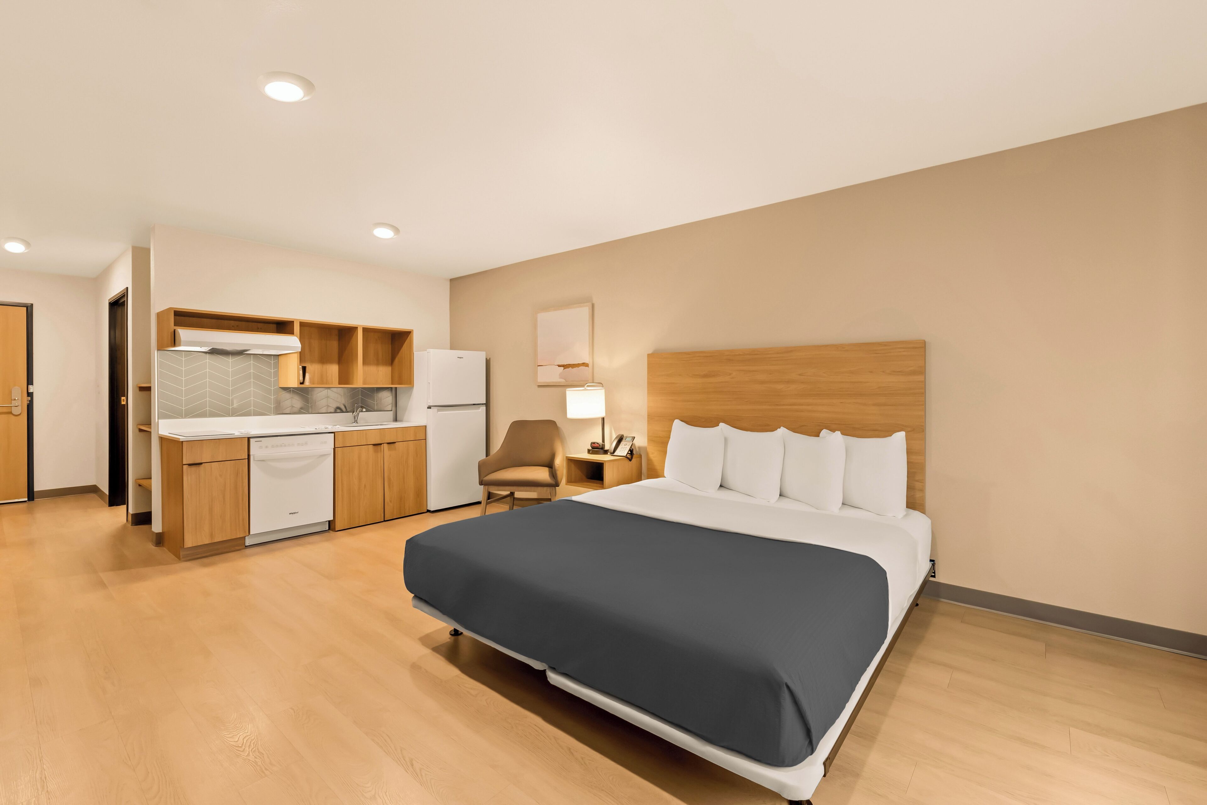 Una habitación de hotel con cama, escritorio, silla, kitchenette y baño.