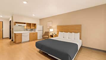Una habitación de hotel con cama, escritorio, silla, kitchenette y baño.