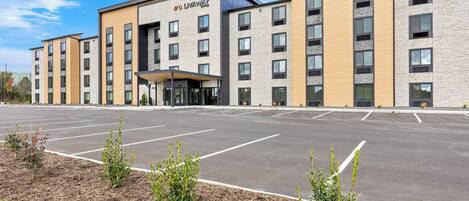 A modern hotel with a flat roof, multiple floors, and a parking lot in front.