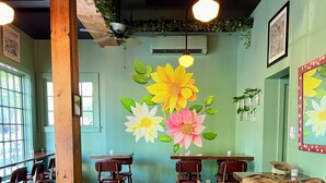 A restaurant interior with wooden floors, green walls, and a mural of flowers. Tables and chairs are arranged for dining.