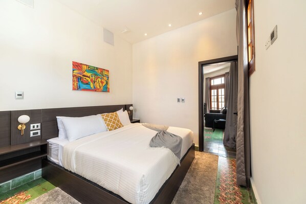 Une chambre d’hôtel moderne avec un grand lit, une table de chevet, une lampe fixée au mur et un tableau coloré.