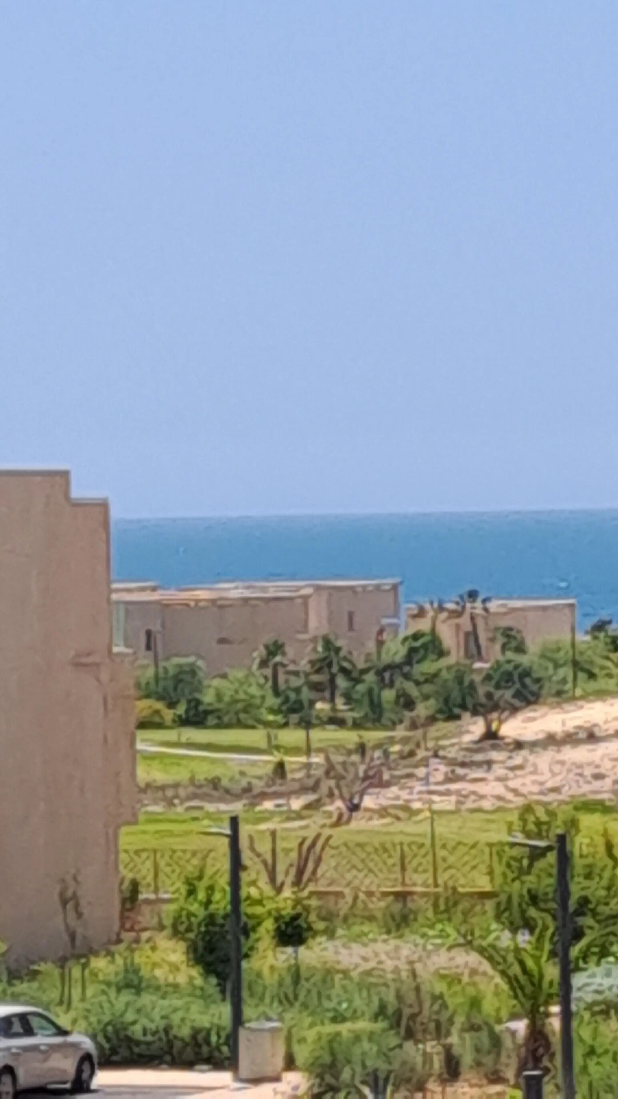 A coastal residential area with buildings, a car, and a view of the sea.