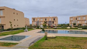 Un complejo residencial moderno con varias edificaciones, un patio central con piscina y jardines bien cuidados.