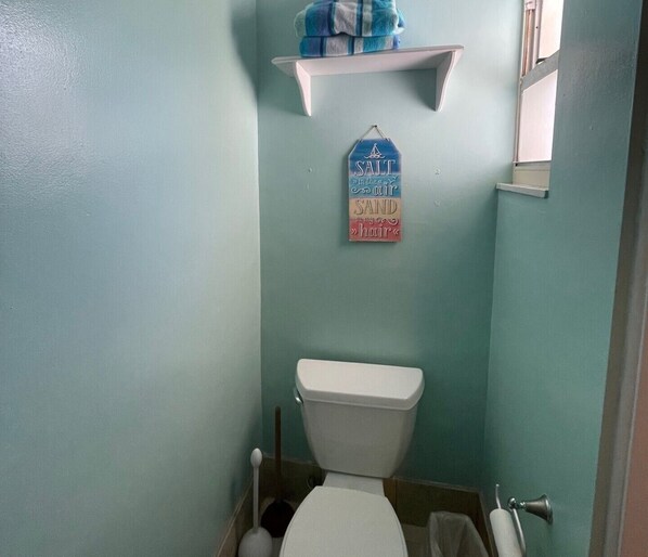 A small bathroom with a toilet, a shelf with towels, and a sign on the wall.
