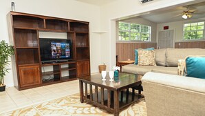 Een woonkamer met een televisie, een houten tv-meubel, een bank en een vloerkleed met een patroon.