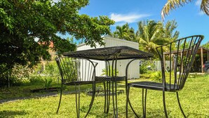Een set metalen tafel en stoelen op een gazon, met een wit gebouw op de achtergrond.