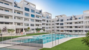 Un moderno edificio de apartamentos con piscina central, varios balcones y un césped bien cuidado.