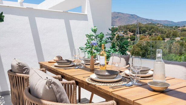 Mesa de madera dispuesta para una comida, con vistas a montañas y vegetación.
