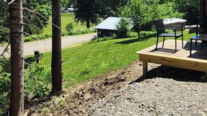 A gravel patio with outdoor furniture, a small shed, and a grassy area with trees. - New 1 bedroom Container cabin with direct trail access (cabin 3) (Errol)