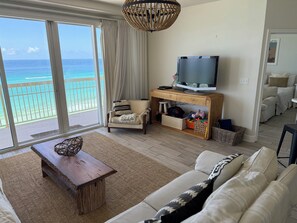 A living room with a large window overlooking the ocean, a wooden TV stand, a sofa, and a coffee table.