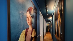 A hallway with wooden flooring, blue walls, and a large framed artwork on the left.