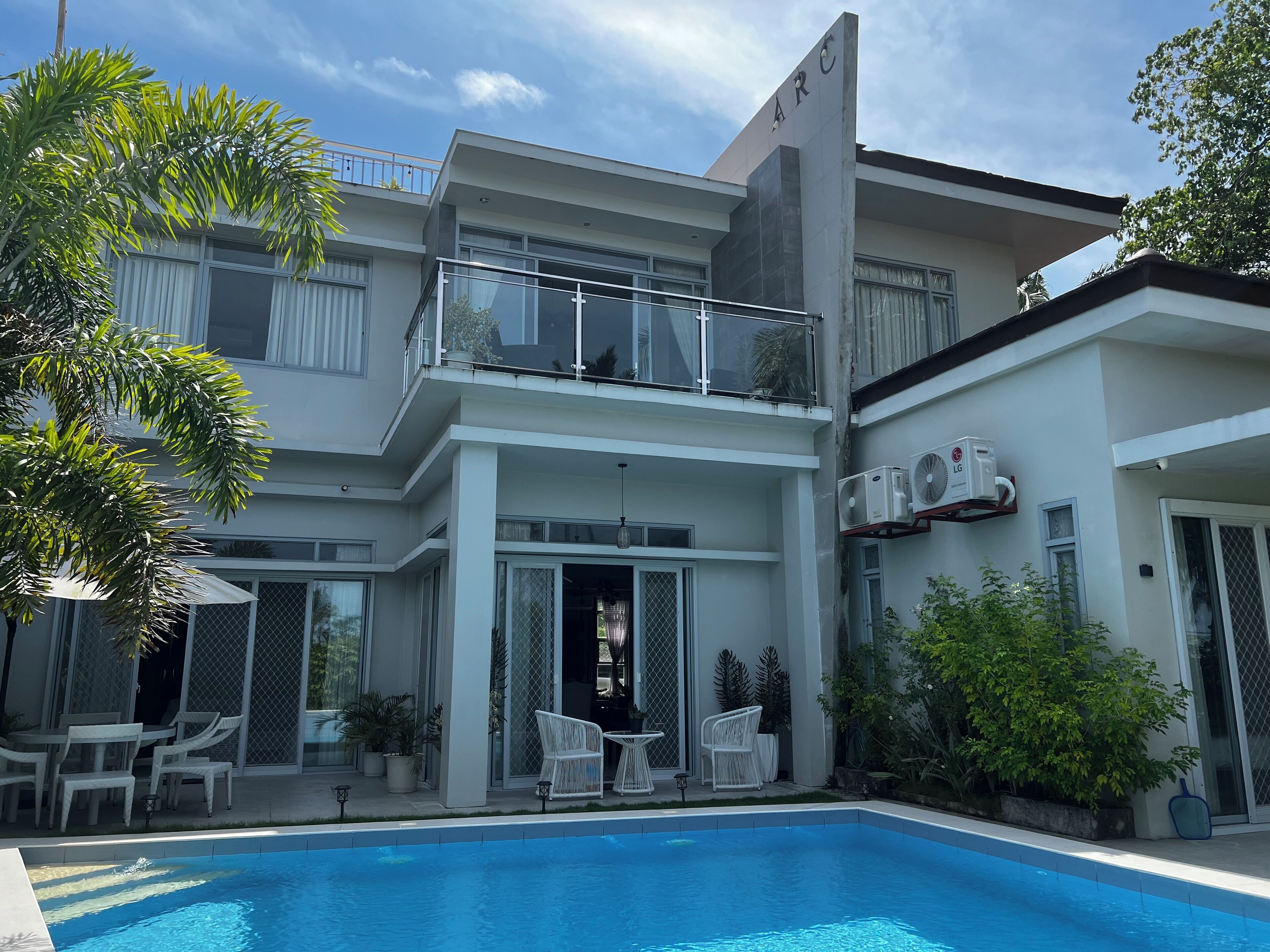 Una casa moderna de dos plantas con piscina, mobiliario exterior y unidades de aire acondicionado.