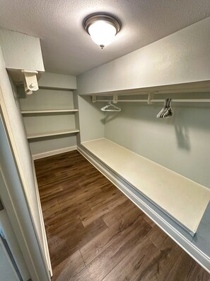 Spacious walk-in closet with a central hanging rod and two shelves for ample storage.
