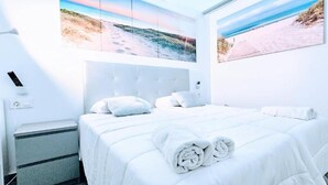 Een hotelkamer met een groot bed, wit beddengoed en twee kunstwerken met een strandthema.