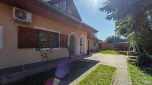 A house with a paved driveway, a small garden, and an air conditioning unit mounted on the exterior wall.