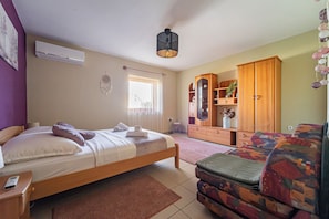 A bedroom with a bed, a wooden wardrobe, a sofa, and a hanging light fixture.