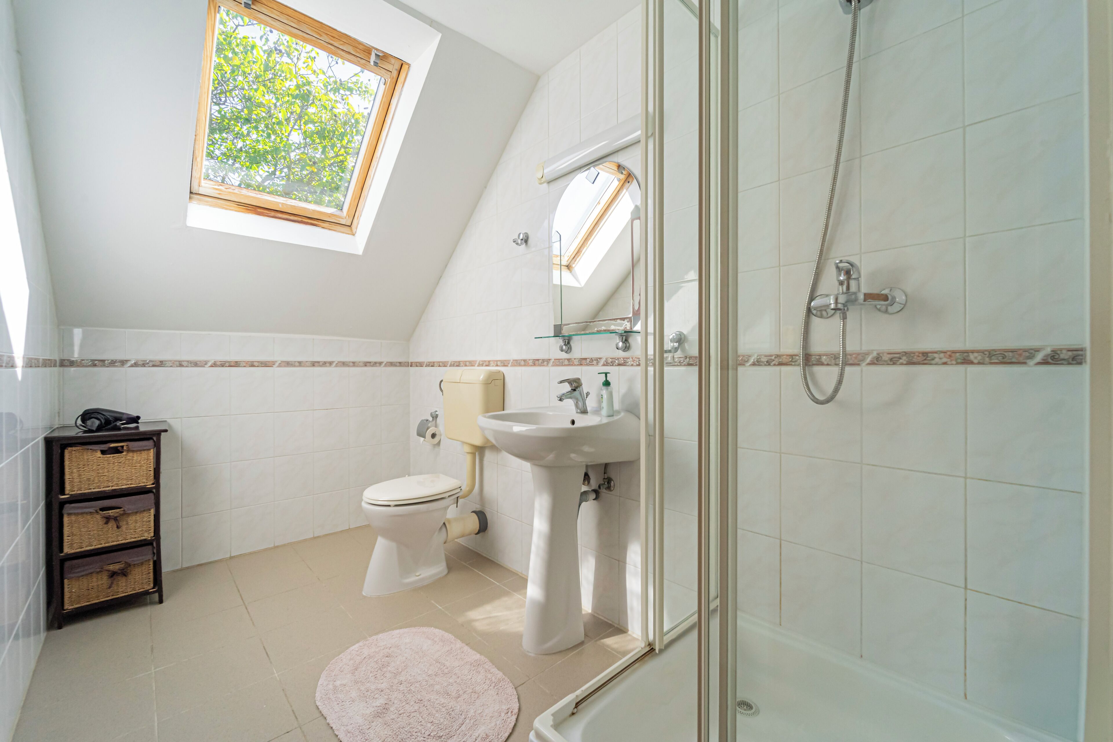 Un baño con tragaluz, inodoro, lavamanos y ducha.