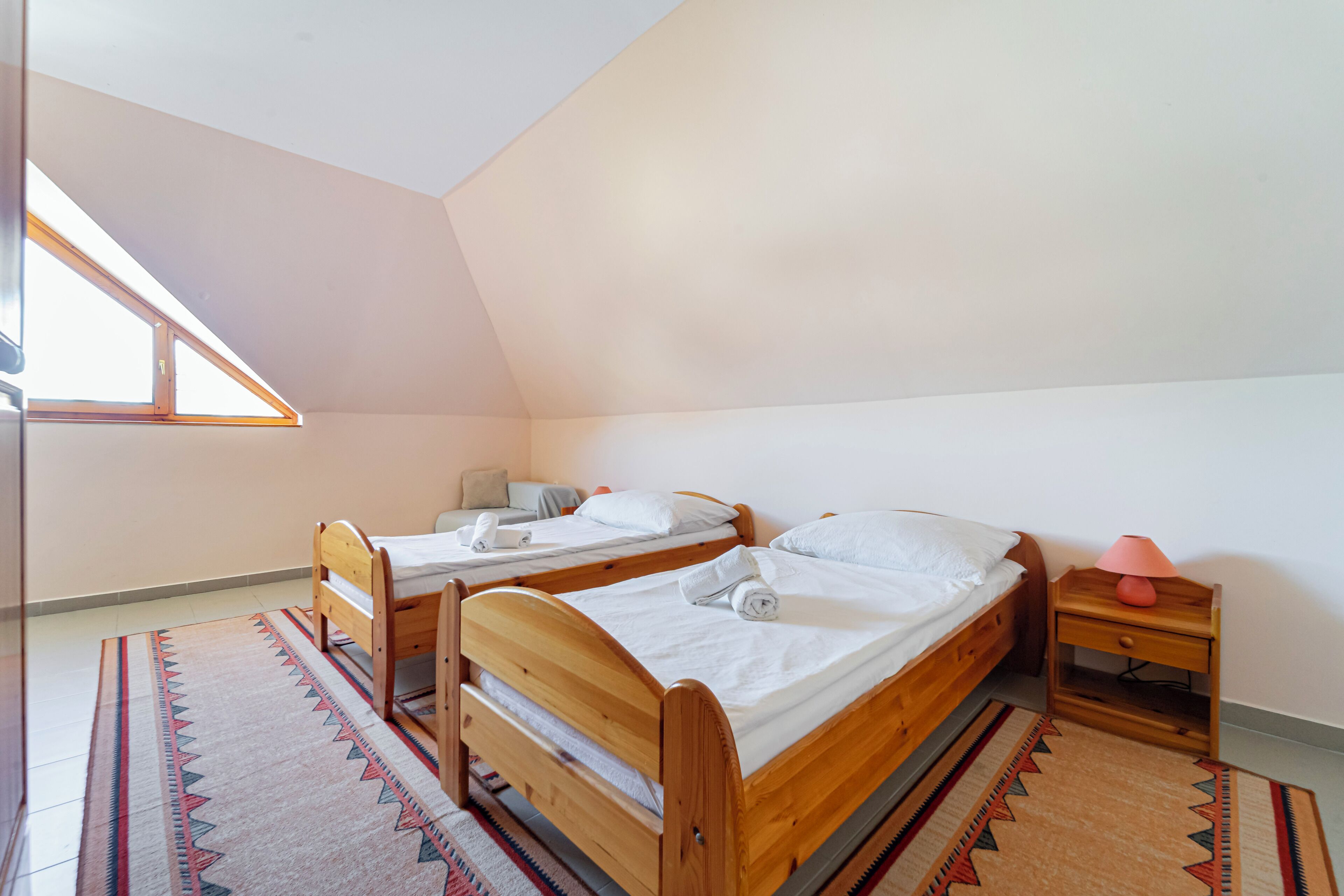 A room with two wooden beds, a nightstand with a lamp, a window, and a patterned rug.