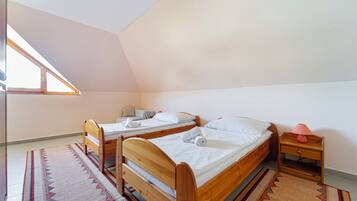 A room with two wooden beds, a nightstand with a lamp, a window, and a patterned rug.
