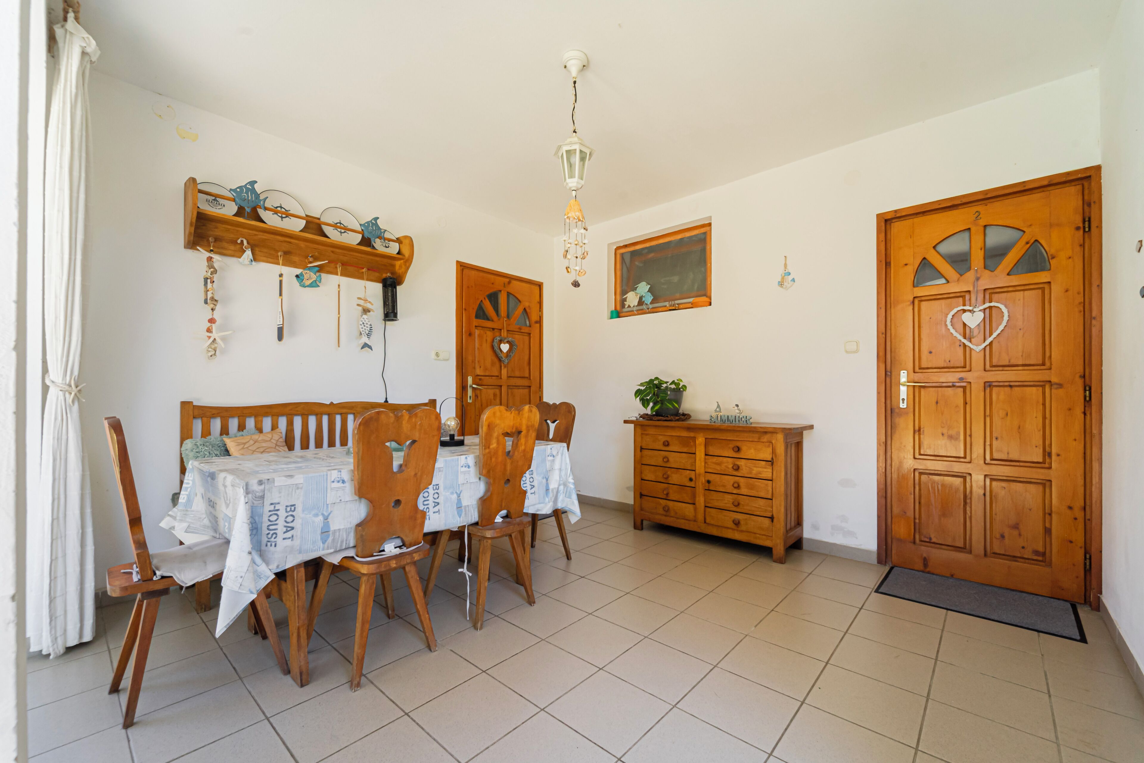 Un coin repas comprenant une table et des chaises en bois, un buffet en bois et une porte ornée d’un motif en forme de cœur.
