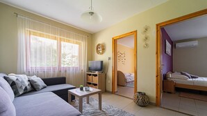 A living room with a sofa, a television, a small table, and a window with curtains.
