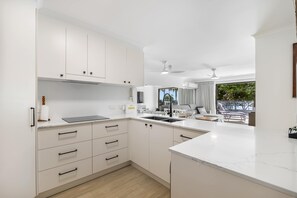 A modern kitchen with white cabinets, a countertop, and a view to a balcony. - Spinnaker 6 Mooloolaba Beach Apt (Mooloolaba)
